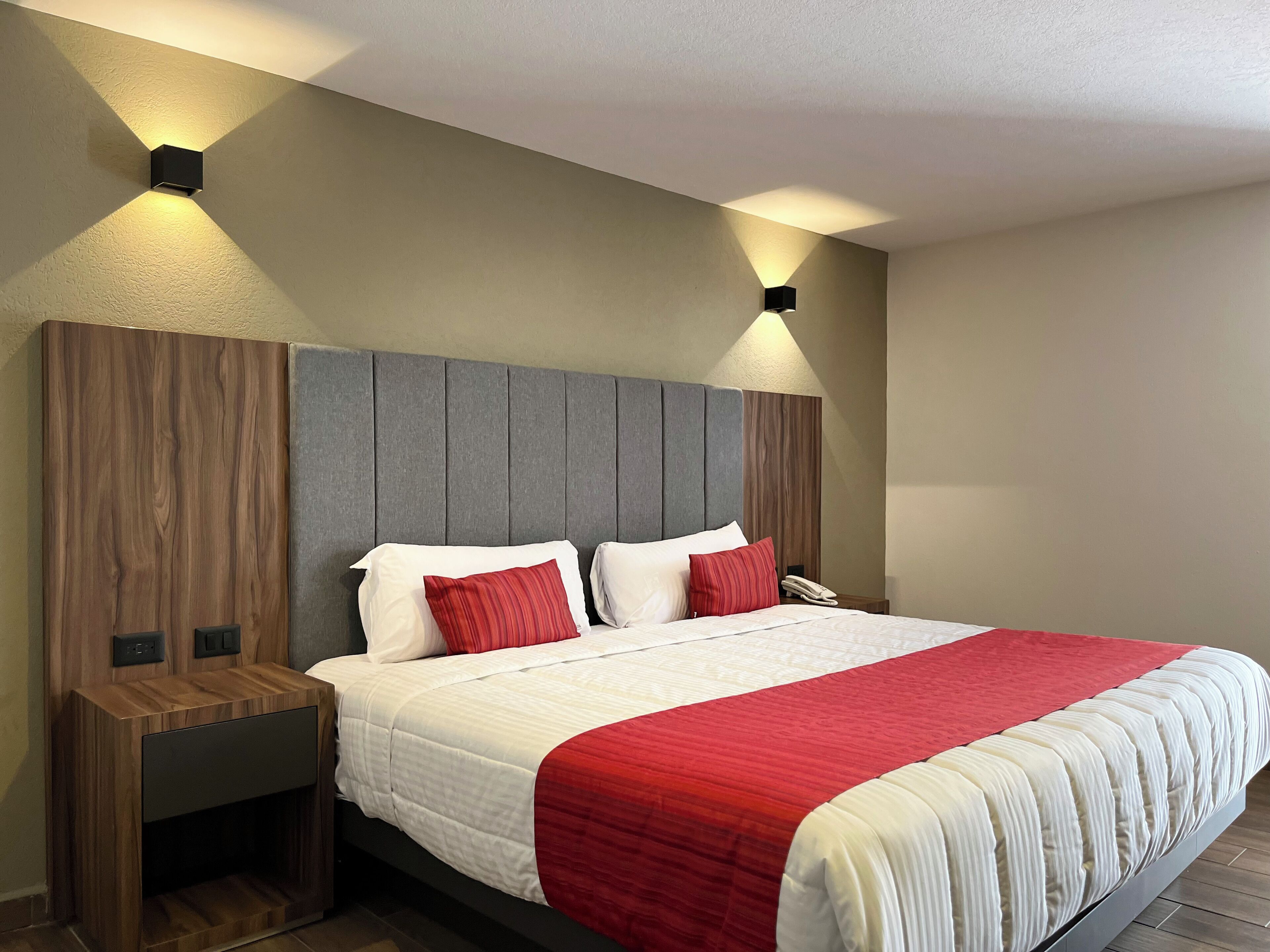 A modern hotel room with a large bed, a wooden nightstand, and two wall-mounted light fixtures.