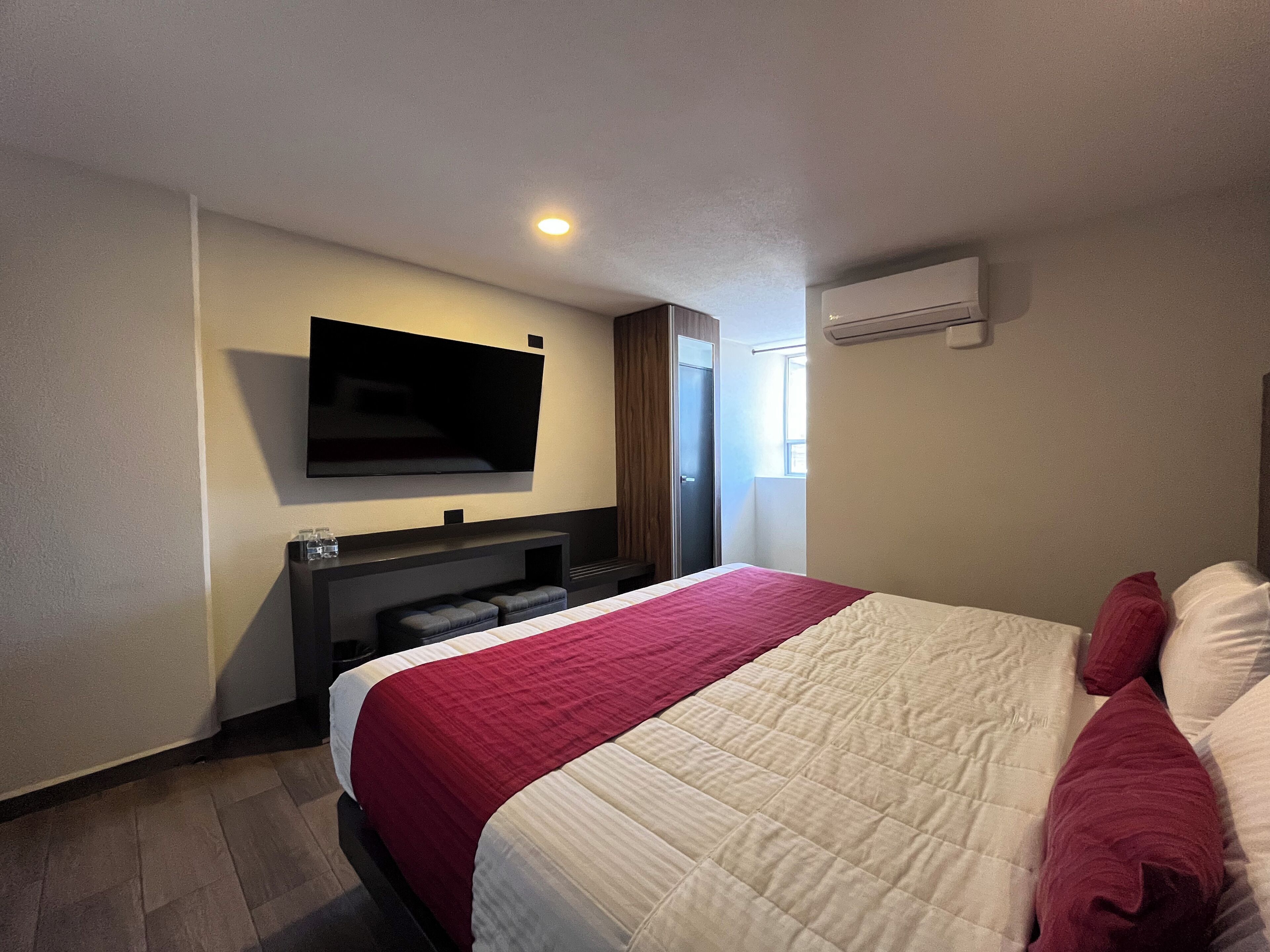Een hotelkamer met een bed, een wandtelevisie, een zithoekje en een airconditioner.