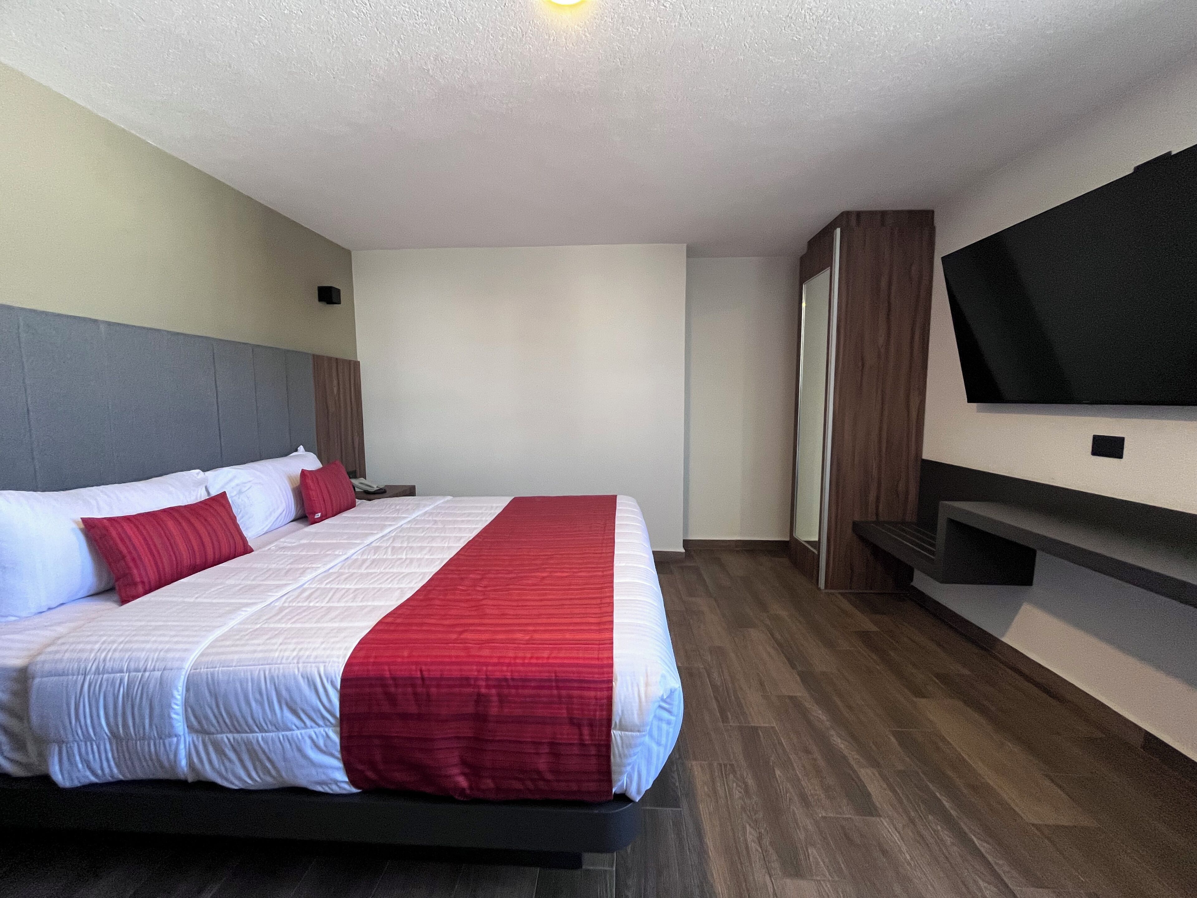 A hotel room with a large bed, a flat-screen TV mounted on the wall, and a wooden floor.