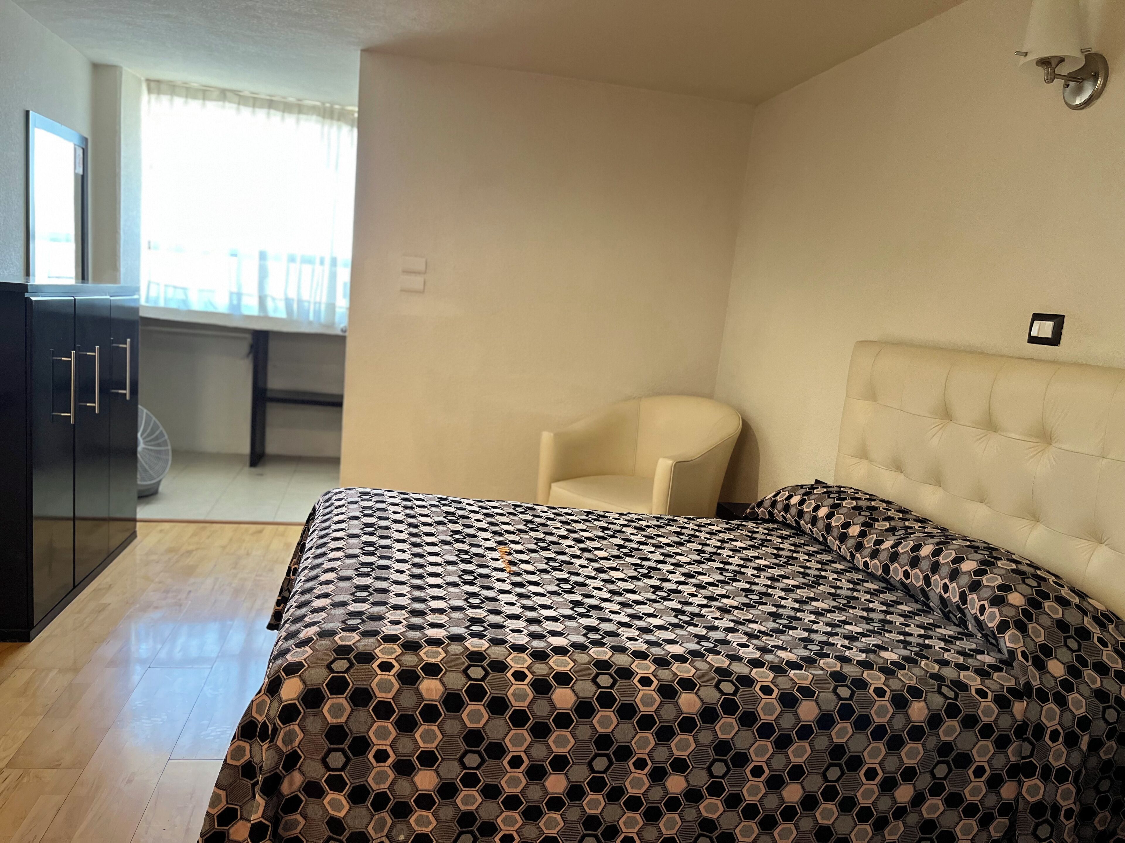 Un dormitorio con cama, una silla, armario y ventana.