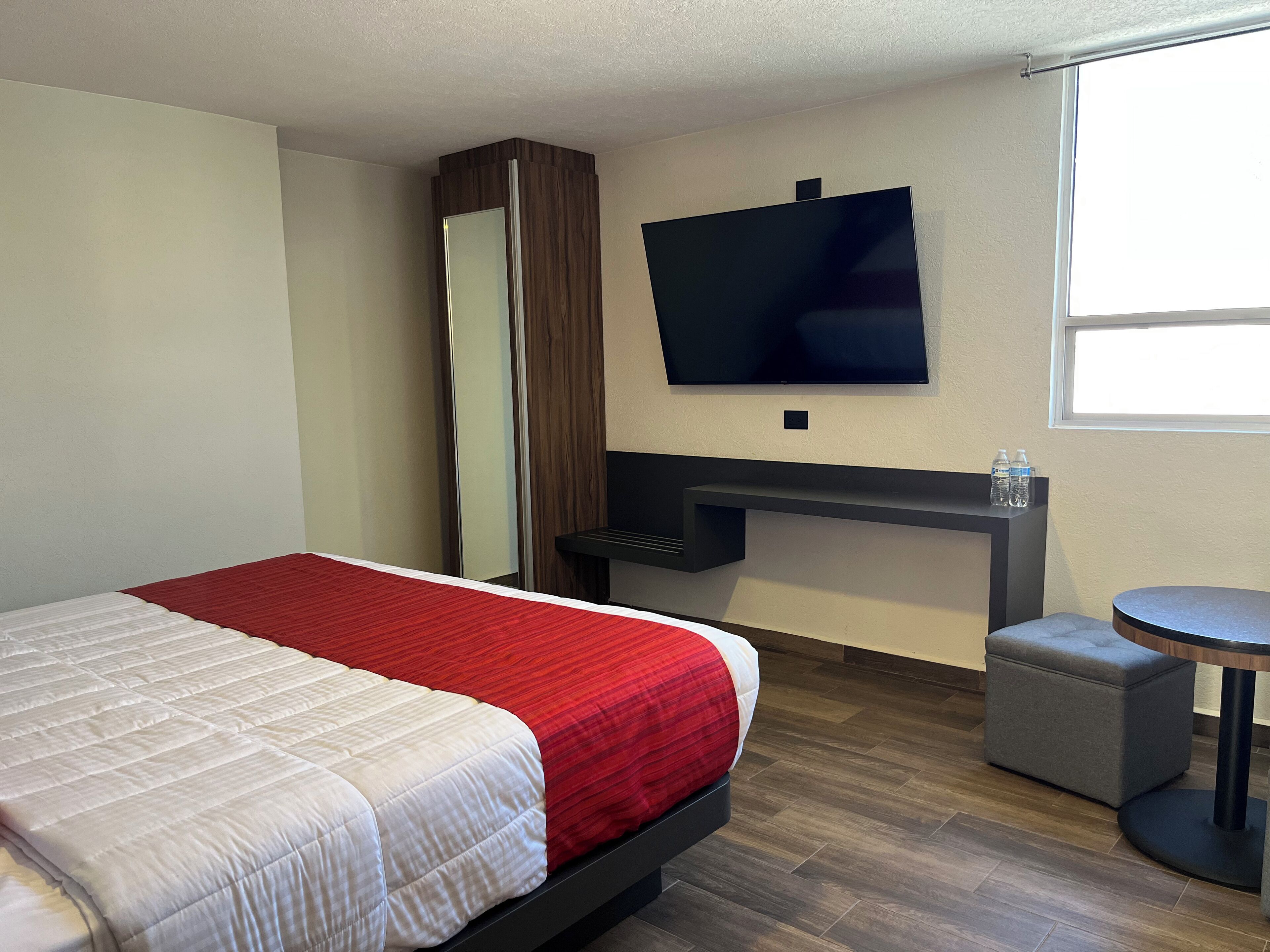 Una habitación de hotel con cama, televisor montado en la pared, un escritorio pequeño y una mesa redonda.