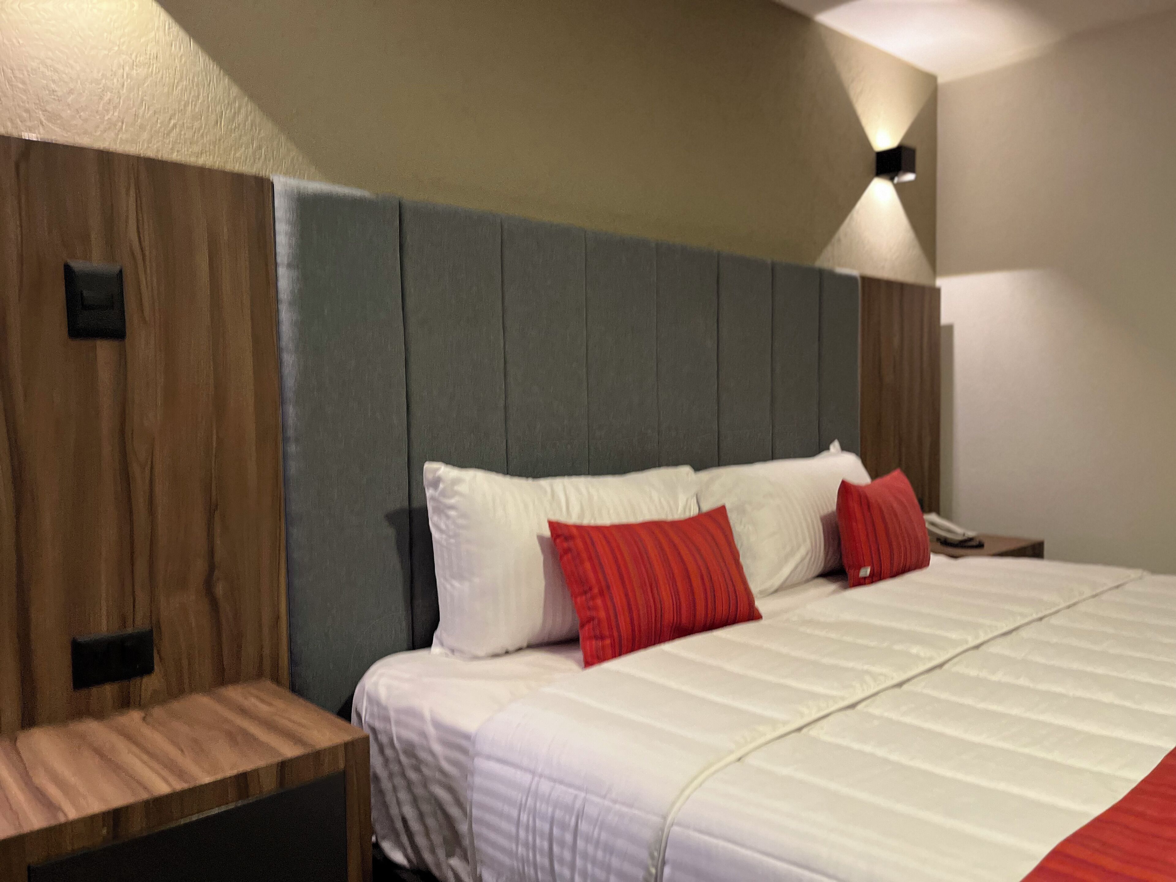 A modern hotel room with a large bed, wooden headboard, and a nightstand.