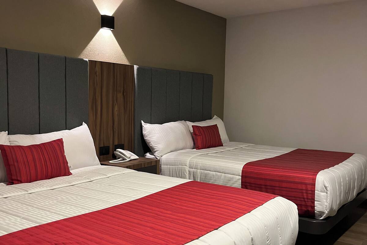 A hotel room with two beds, each with white and red bedding, a wooden headboard, and a bedside telephone.