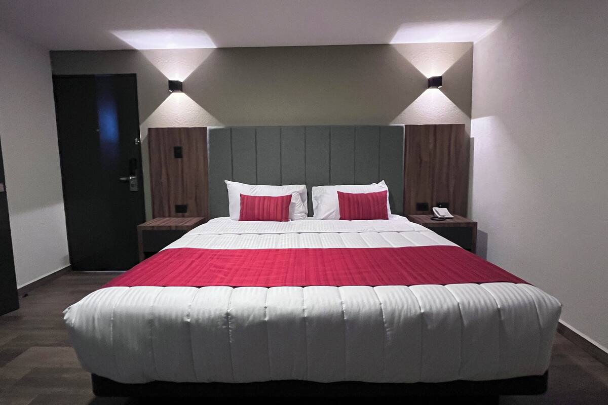 A neatly made bed with a red and white bedspread, two bedside lamps, and a wooden headboard.