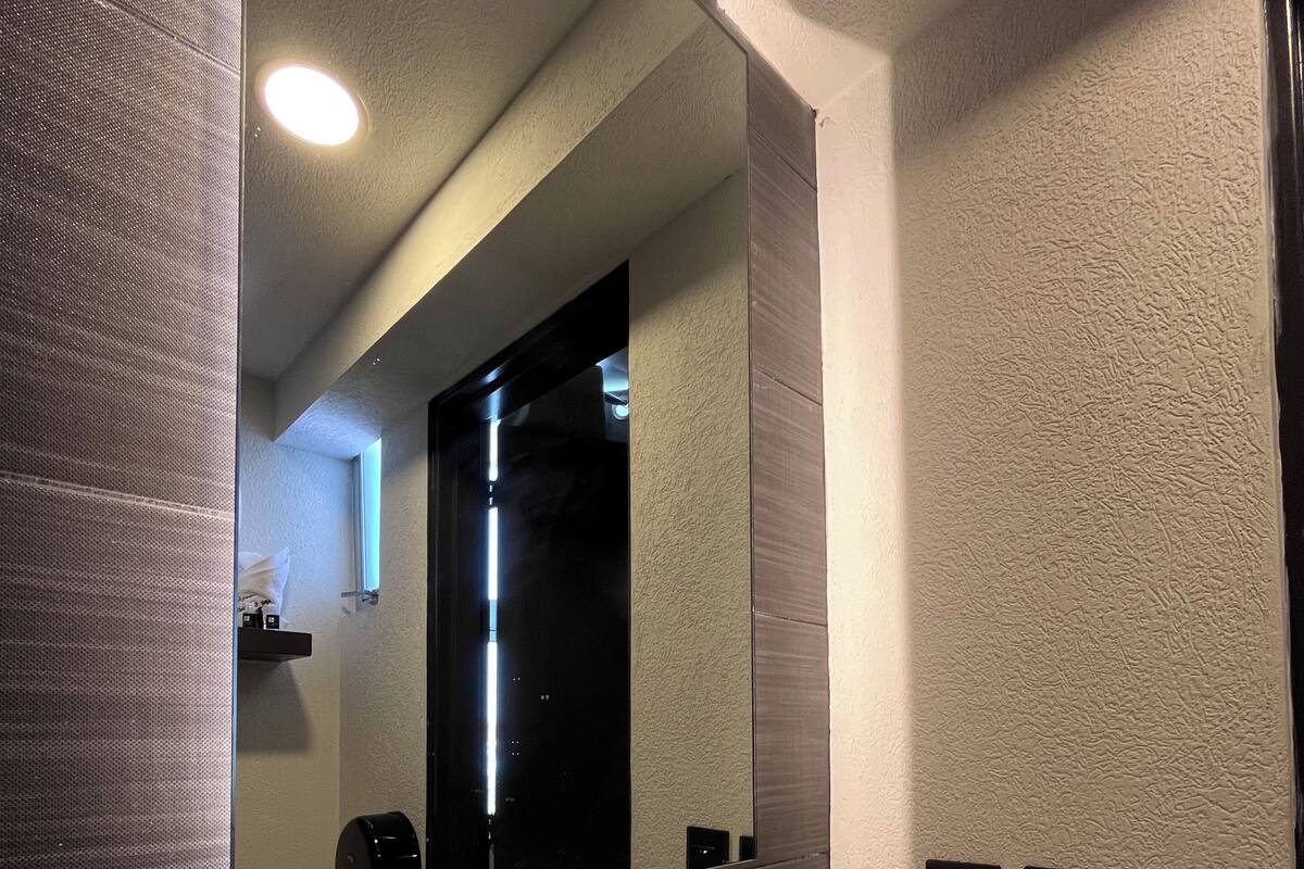 A modern bathroom with a white sink, a large mirror, and a textured wall.