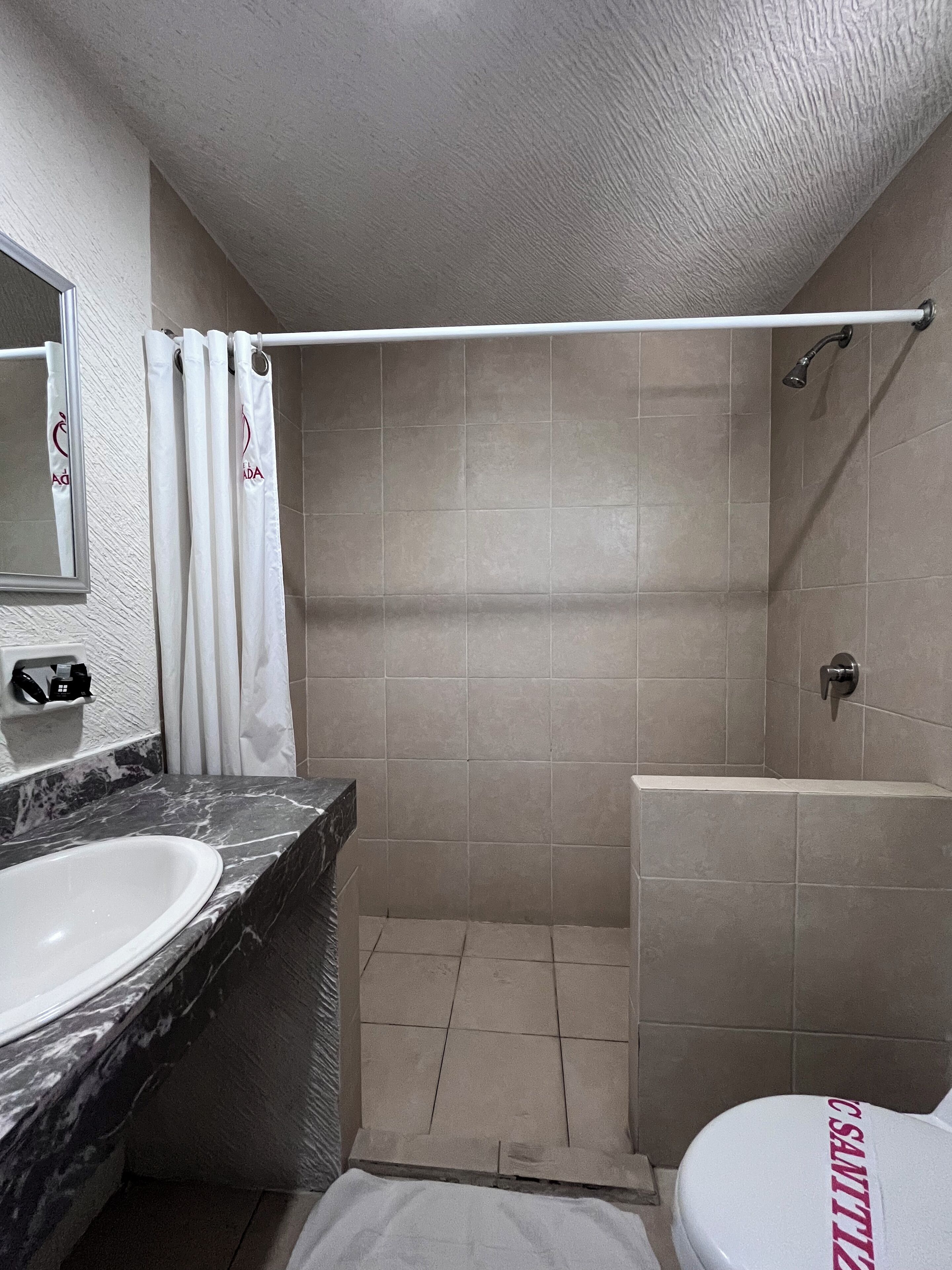 A bathroom with a marble sink, a toilet with a red logo, and a shower area.