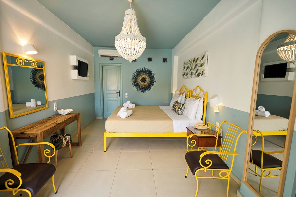 Quarto de hotel com cama, escrivaninha, cadeira, espelho e lustre.