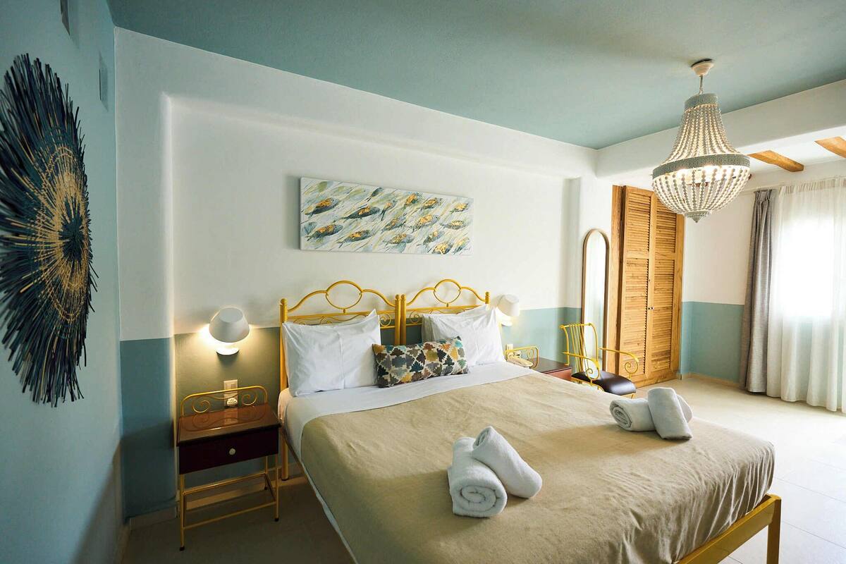 Um quarto bem arrumado com cama, mesas de cabeceira, uma luminária na parede e um candelabro.