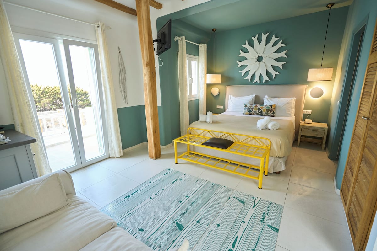 Quarto com cama, mesas de cabeceira, televisão, janela com cortinas e vista exterior.