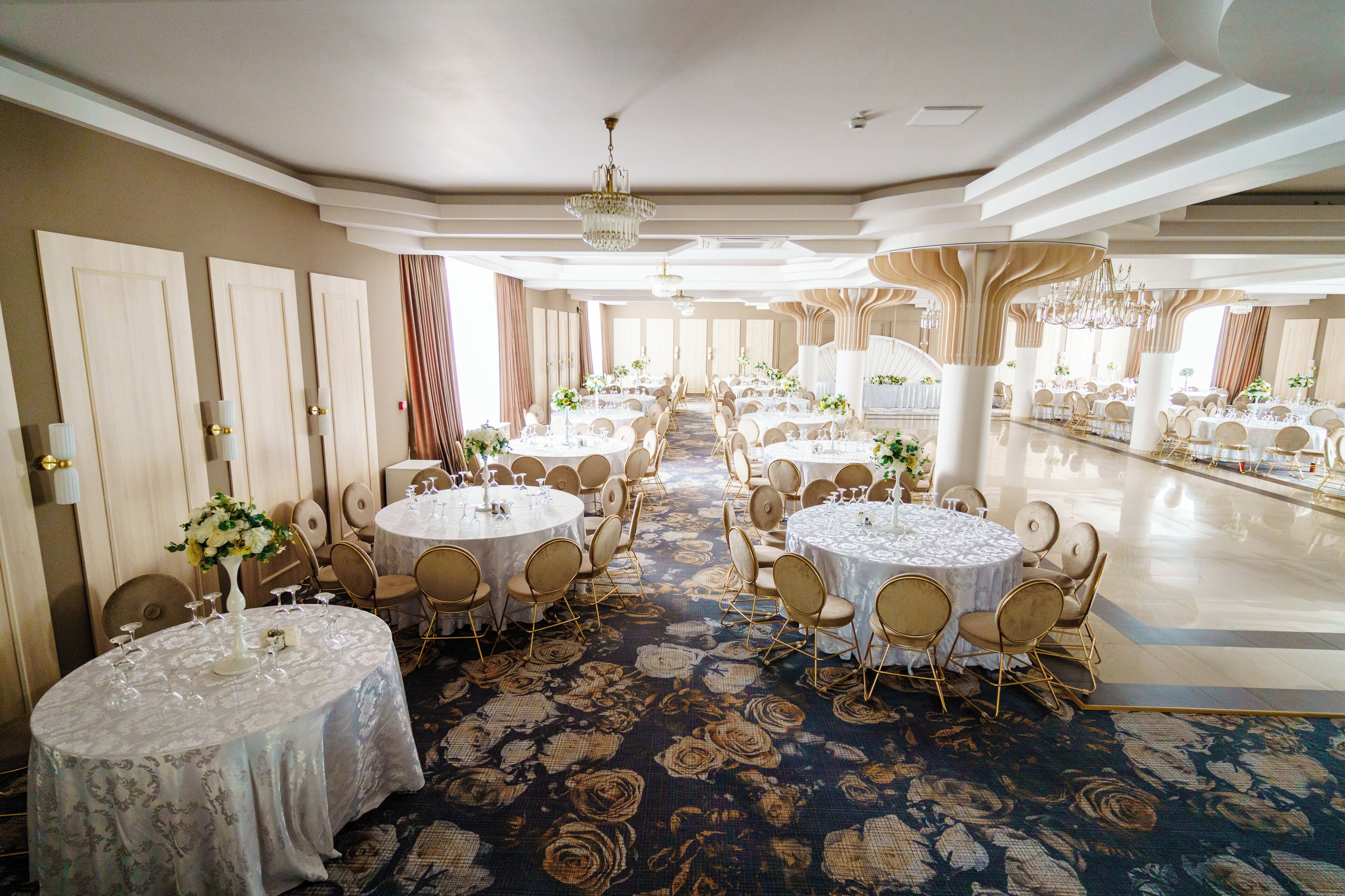 A banquet hall with round tables, chairs, and chandeliers.