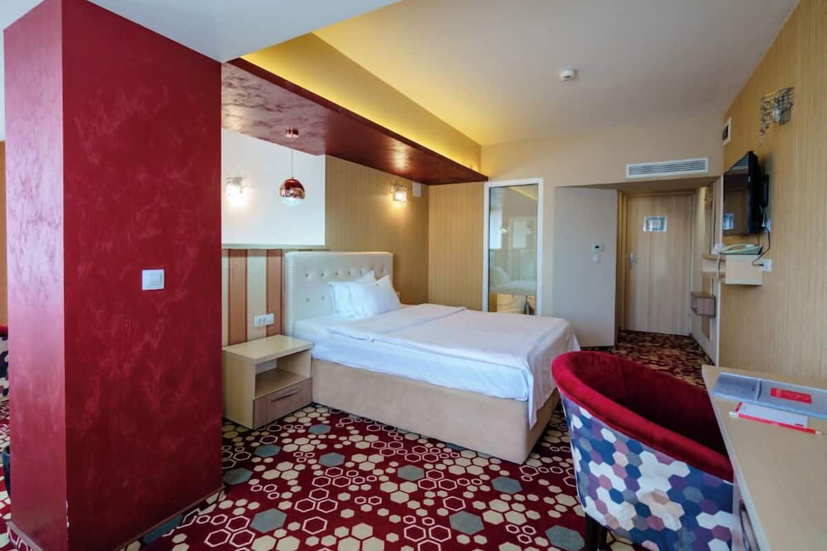 Habitació d'hotel amb un llit, una taula de nit i una cadira vermella.