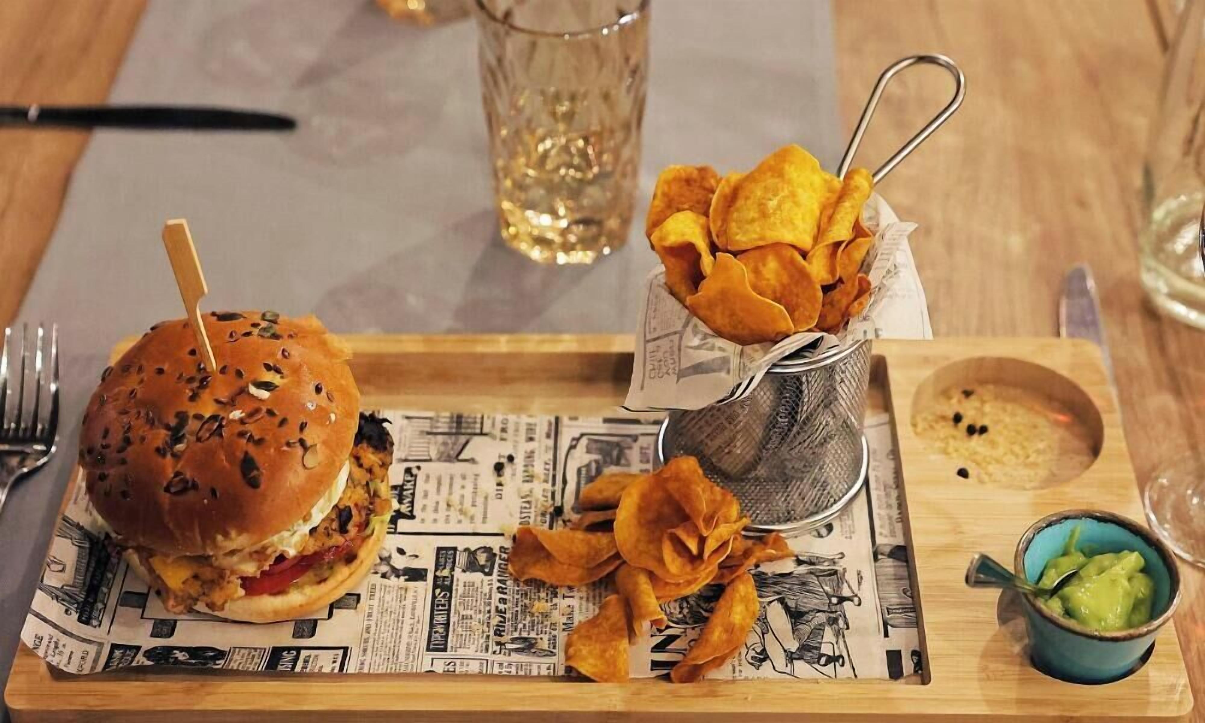 Un vassoio con un hamburger, patatine e una piccola ciotola di salsa, su un tavolo rivestito di giornale.