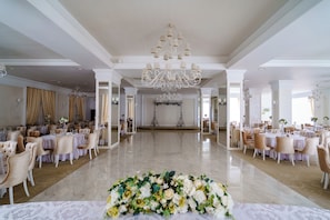 Un salón espacioso con suelo de mármol, elegantes candelabros y filas de mesas con sillas, lo que sugiere un ambiente para un evento formal.