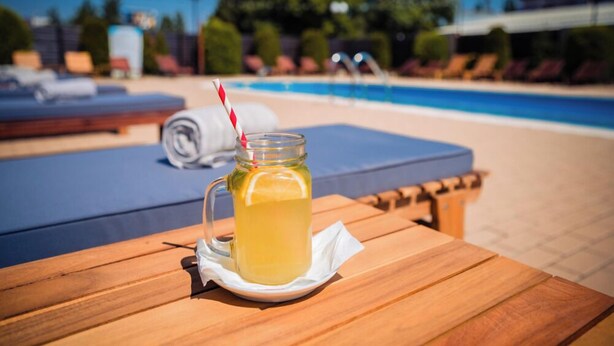 A wooden table with a glass pitcher of lemonade, a striped straw, and a napkin. - Hotel Craiovita (Craiova)