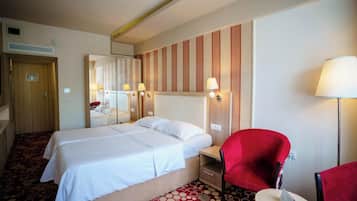 Una camera d'albergo con un letto, una poltrona rossa, un tavolino, uno specchio e una lampada.