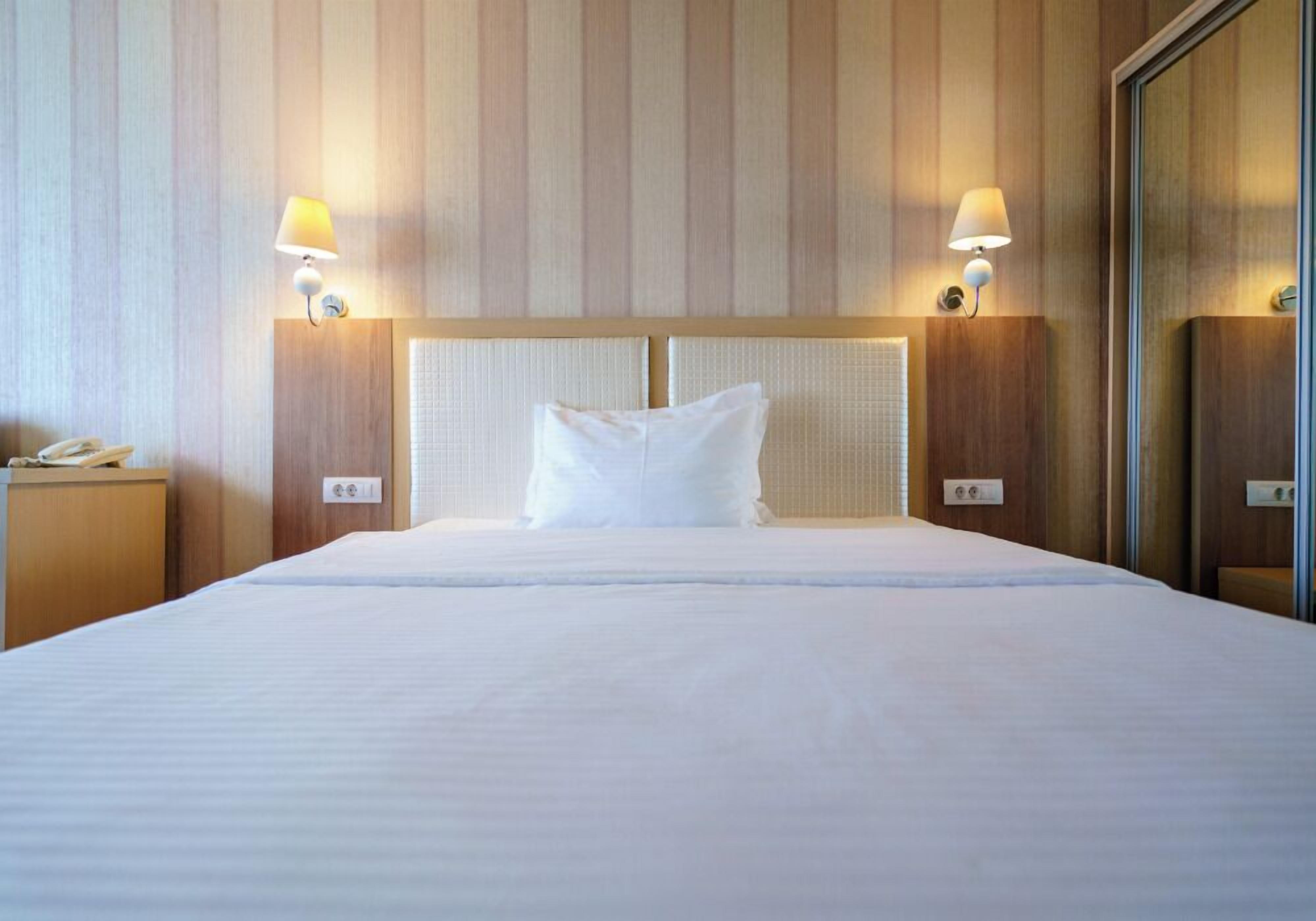 A hotel room with a large bed, two bedside lamps, a nightstand with a phone, and a wooden headboard.