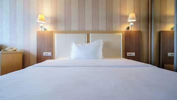 A hotel room with a large bed, two bedside lamps, a nightstand with a phone, and a wooden headboard.