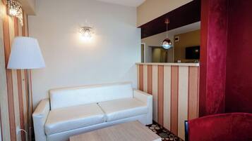 A room with a white sofa, a small table, a red chair, a lamp, and a wall-mounted light fixture.