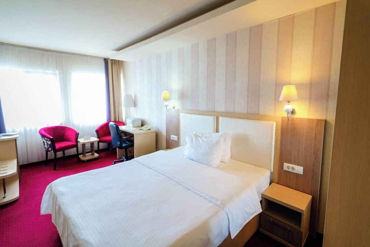 Habitació d'hotel amb un llit, una taula, dues cadires, una làmpada i una finestra amb cortines.