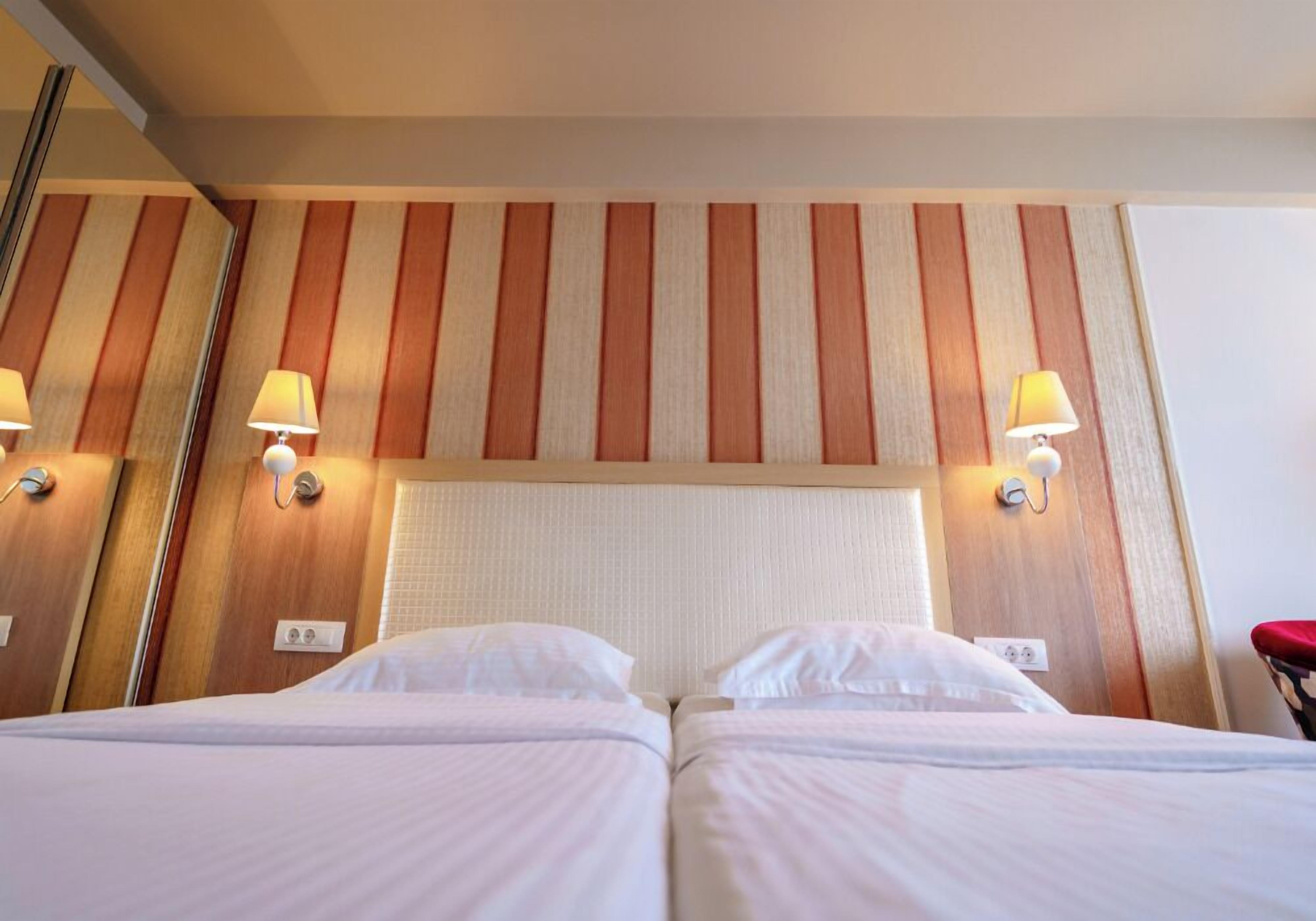A hotel room with two beds, a striped wall, and wall-mounted lamps.