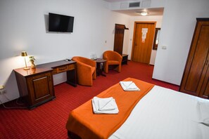 A hotel room with a bed, a desk, two chairs, a television, and a door. - Hotel Elyon Dej (Dej)