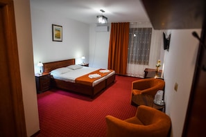 A hotel room with a bed, a desk, a chair, and a large window with curtains. - Hotel Elyon Dej (Dej)