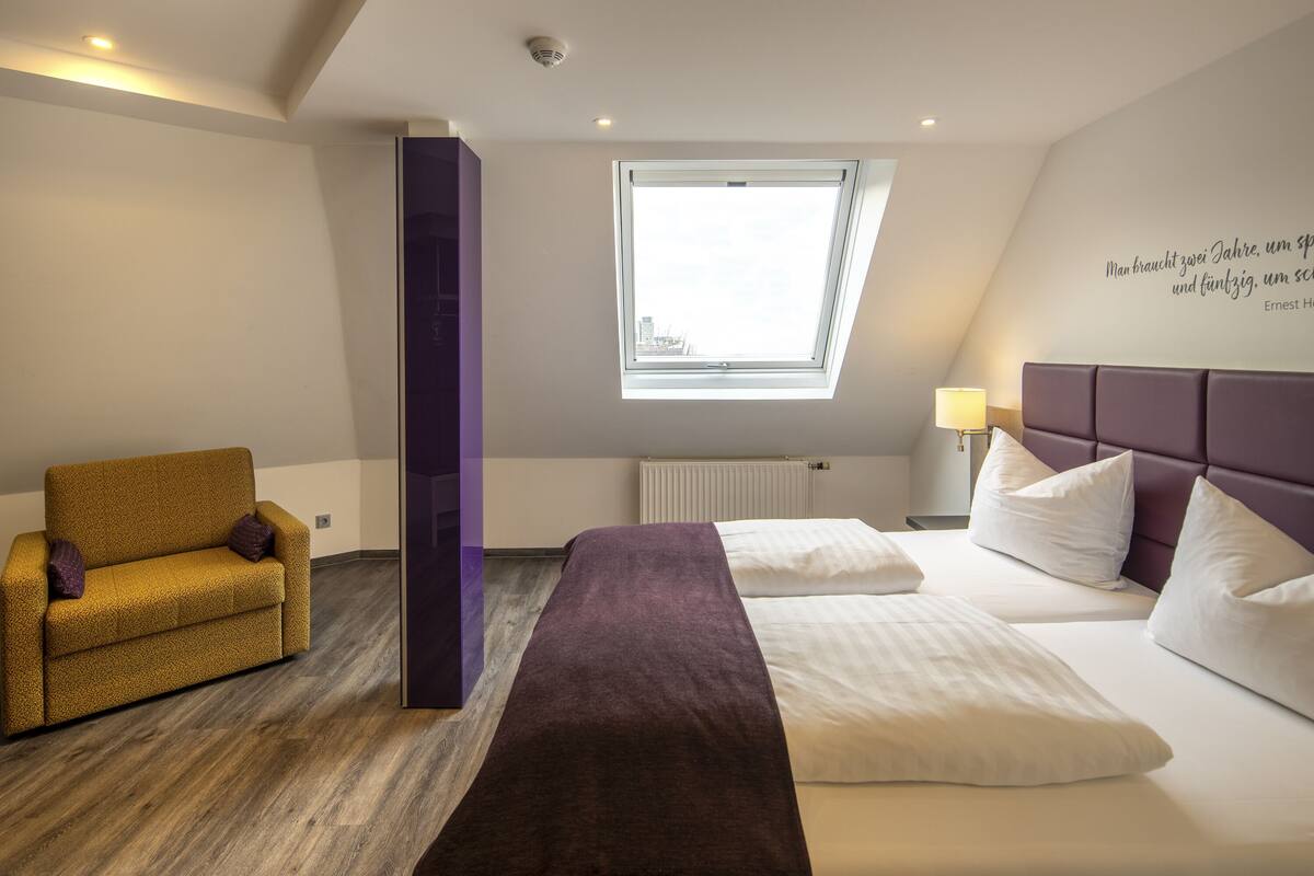Ein Hotelzimmer mit Bett, Sofa, Fenster und Wand mit einem Zitat.