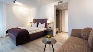 A hotel room with a bed, bedside tables, a small table with a vase, and a sofa. - Hotel Gloria (Stuttgart)