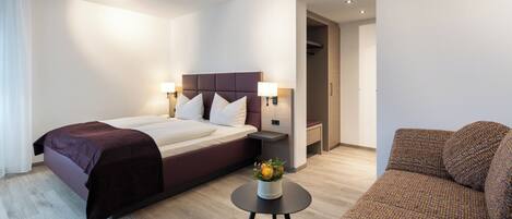 Una habitación de hotel con una cama, mesitas de noche, una pequeña mesa con un florero y un sofá.
