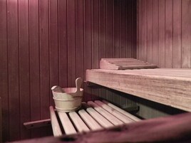 A sauna with wooden benches and a small bucket.