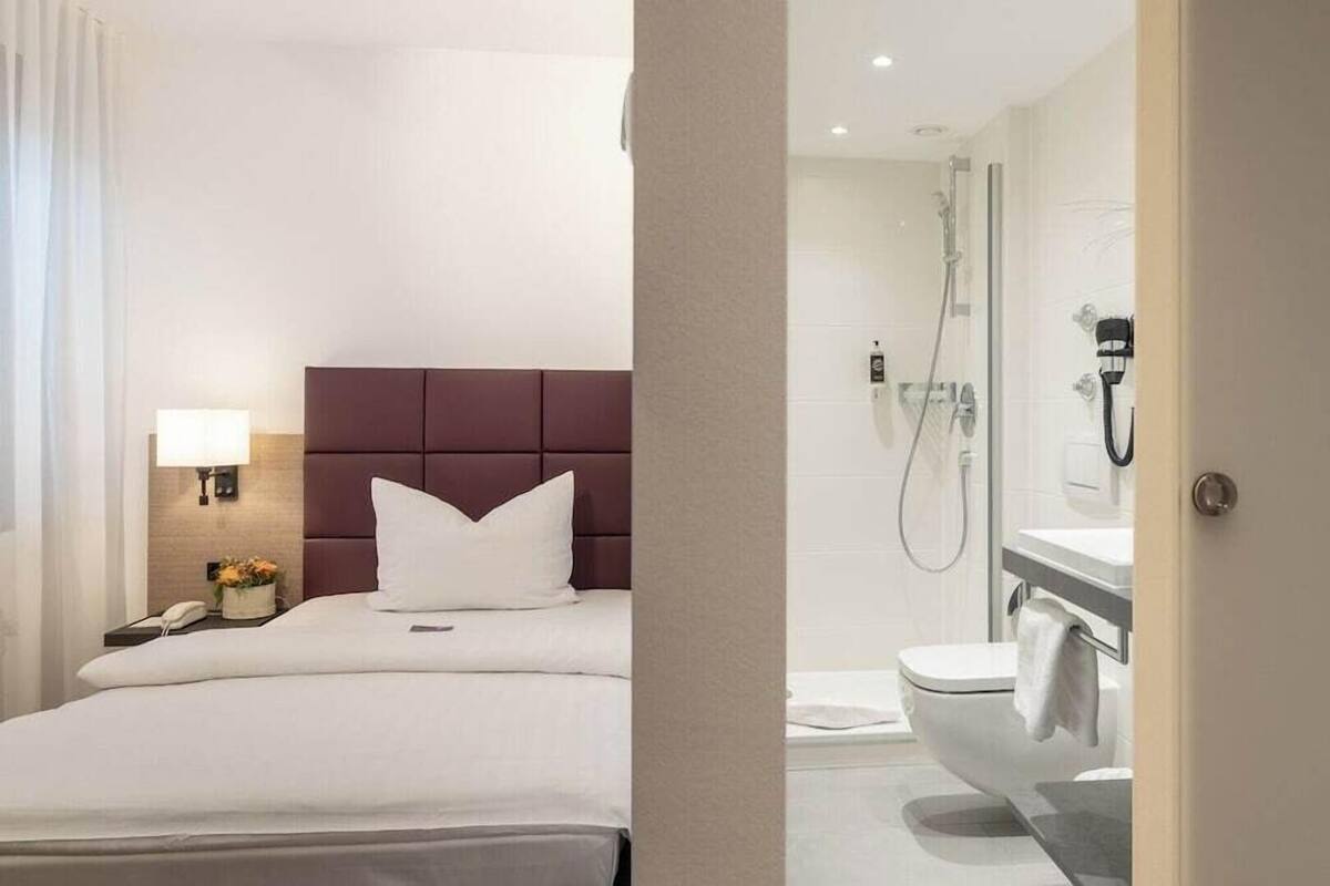 Ein Hotelzimmer mit einem Bett, einem Nachttisch mit Lampe, einem Badezimmer mit Dusche und Toilette.