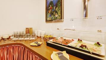 A buffet setup with various food items, including fruits, cheeses, and meats, arranged on a table with a painting above.