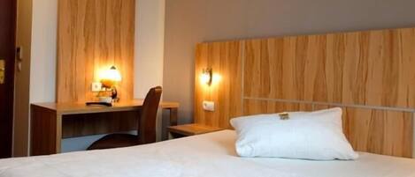 A hotel room with a wooden headboard, a desk with a lamp, and a bed with a pillow.