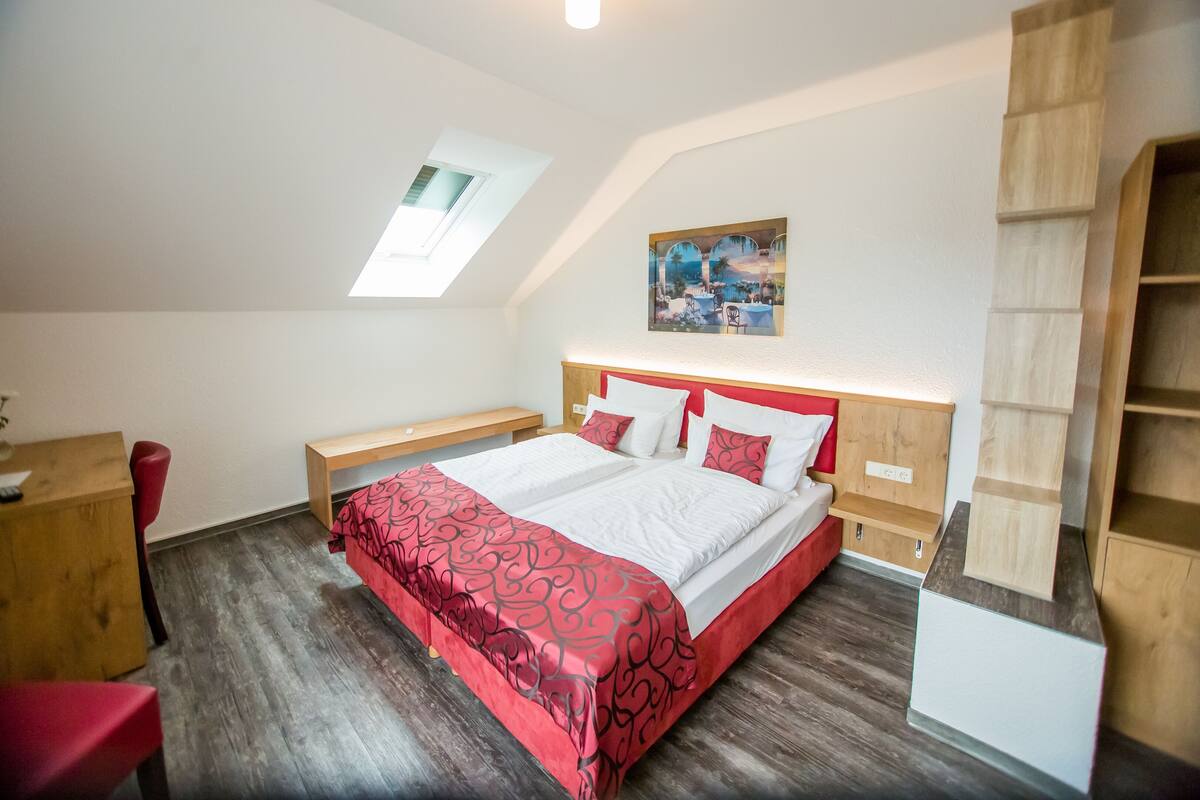 Un dormitorio con una cama grande, un escritorio y una silla. Hay un tragaluz sobre la cama y un cuadro en la pared.