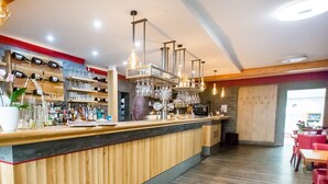 Un'area bar con banconi in legno, mensole con bottiglie e bicchieri, e lampade a sospensione.