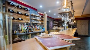 Un'area bar con scaffali pieni di bottiglie e bicchieri, tavoli di legno e un lampadario moderno.