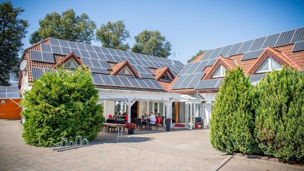 Un edificio con diversi pannelli solari sul tetto, una zona relax all'aperto coperta e un giardino curato.