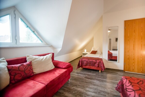 Una habitación con un sofá rojo, una cama con colcha estampada, una puerta de madera y un espejo grande en la pared.