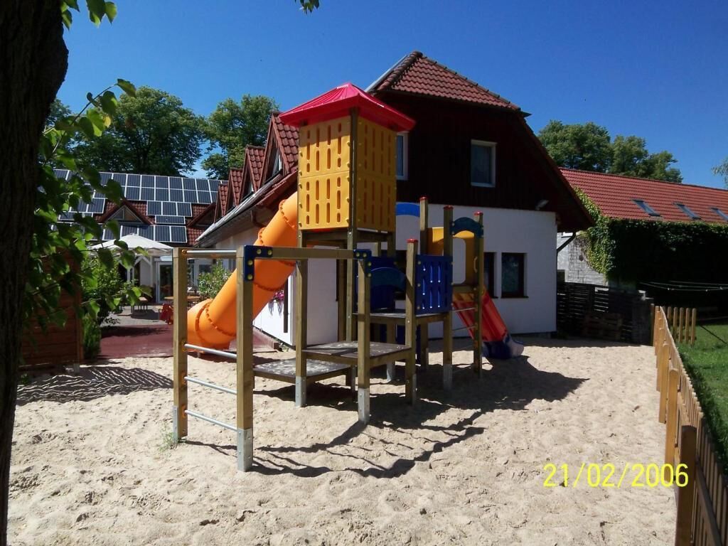 A playground with a slide and climbing structures, a house with a red roof, and solar panels in the background.