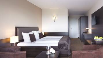 Ein Hotelzimmer mit einem großen Bett, einem Nachttisch mit Lampe, einem kleinen Tisch mit einer Vase und einem Sessel.