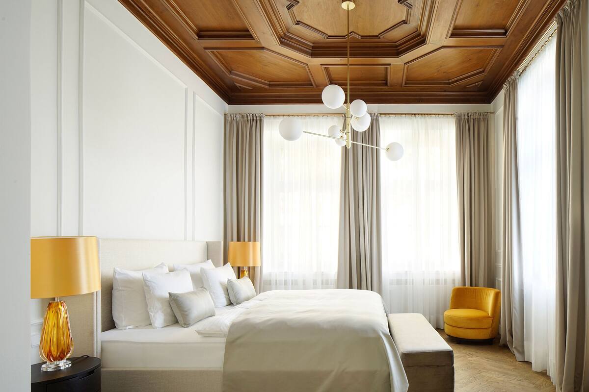 A hotel room with a large bed, a bedside table with a lamp, a bench, and a chair.
