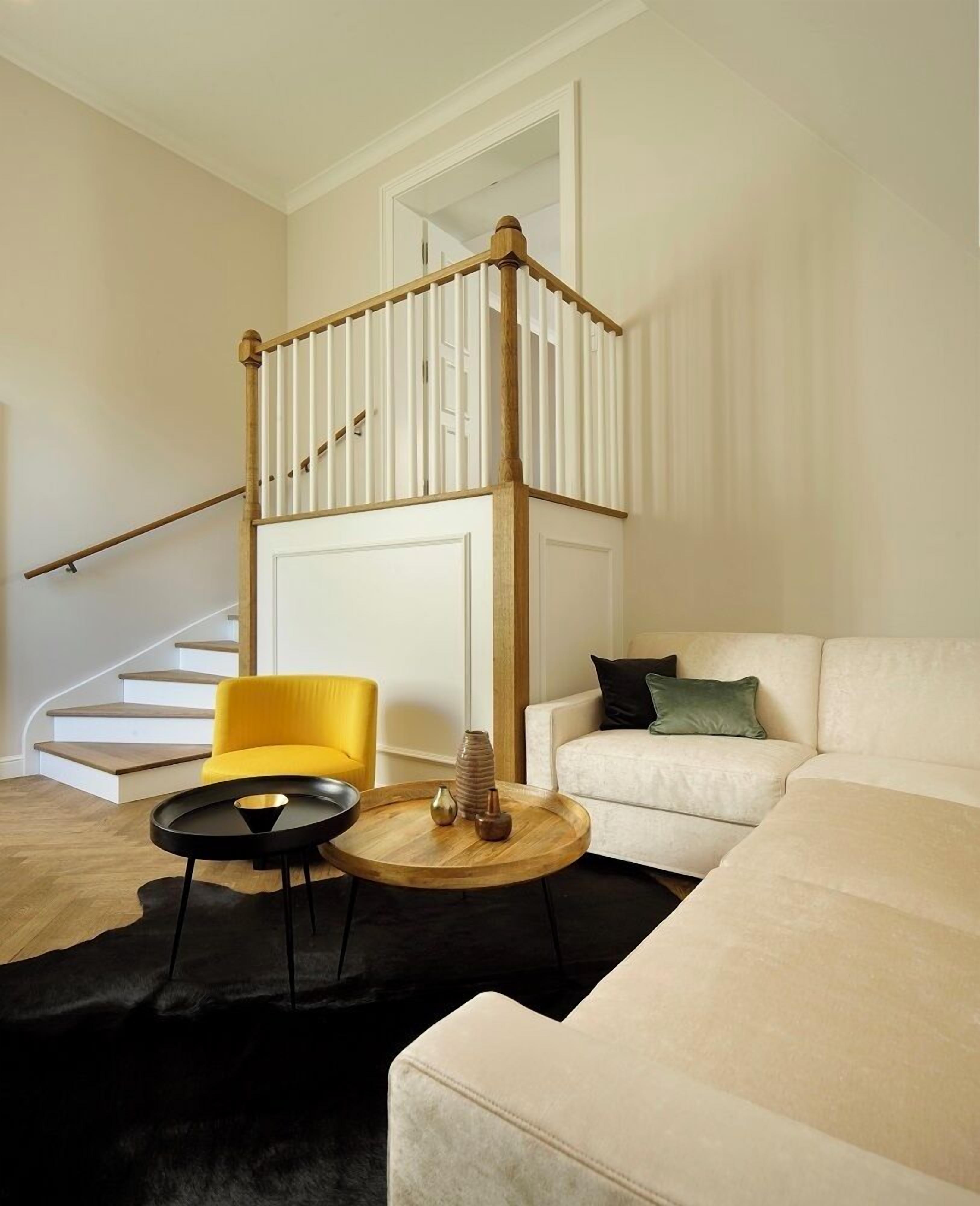 Un salon moderne avec un escalier, un fauteuil jaune, un canapé blanc et une table basse ronde en bois.