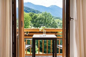 A balcony with a wooden table and chairs, a vase with flowers, and a view of a forested mountain range. - Das Tegernsee (Tegernsee)