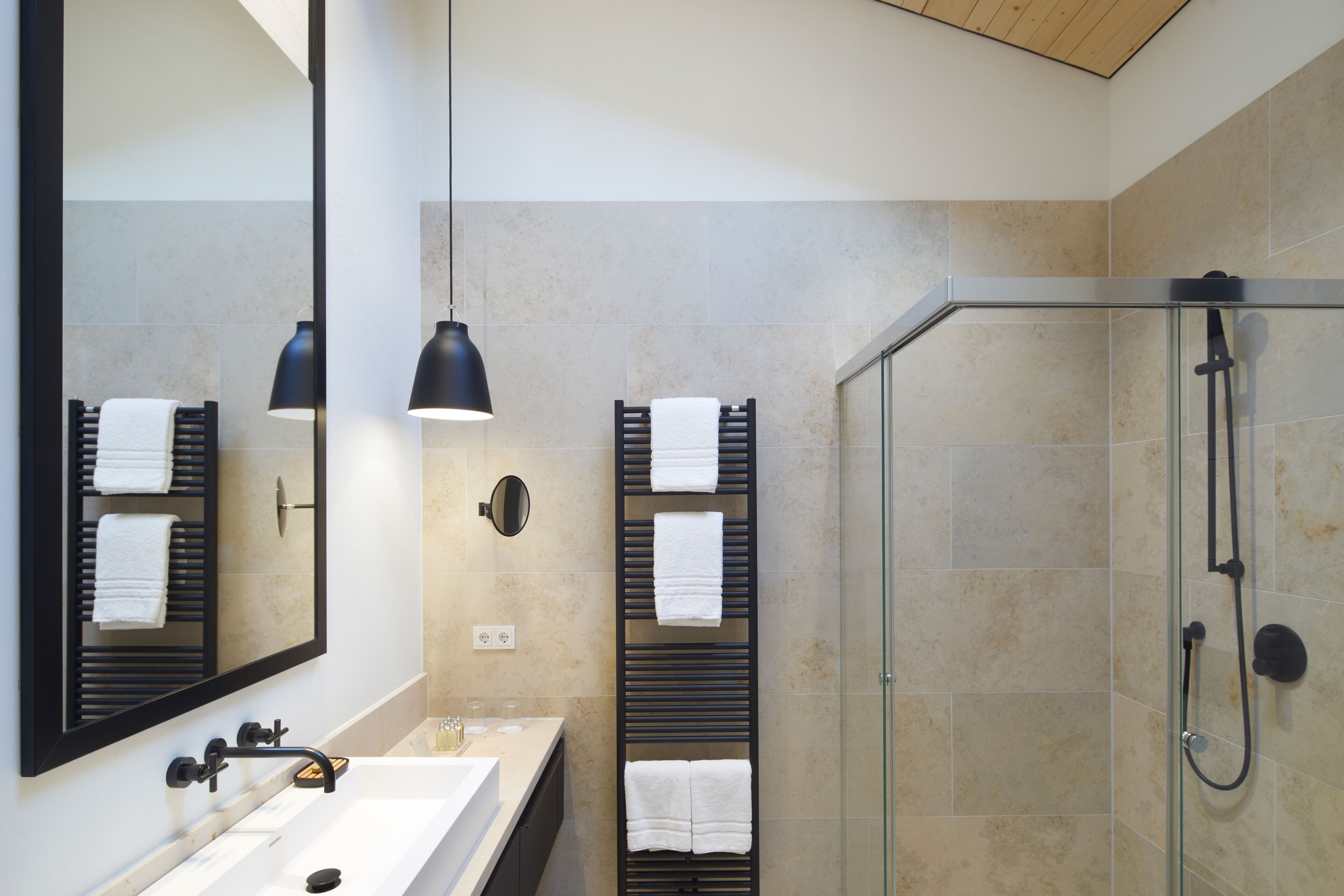 A modern bathroom with a large mirror, two pendant lights, a glass shower enclosure, and multiple towel racks.