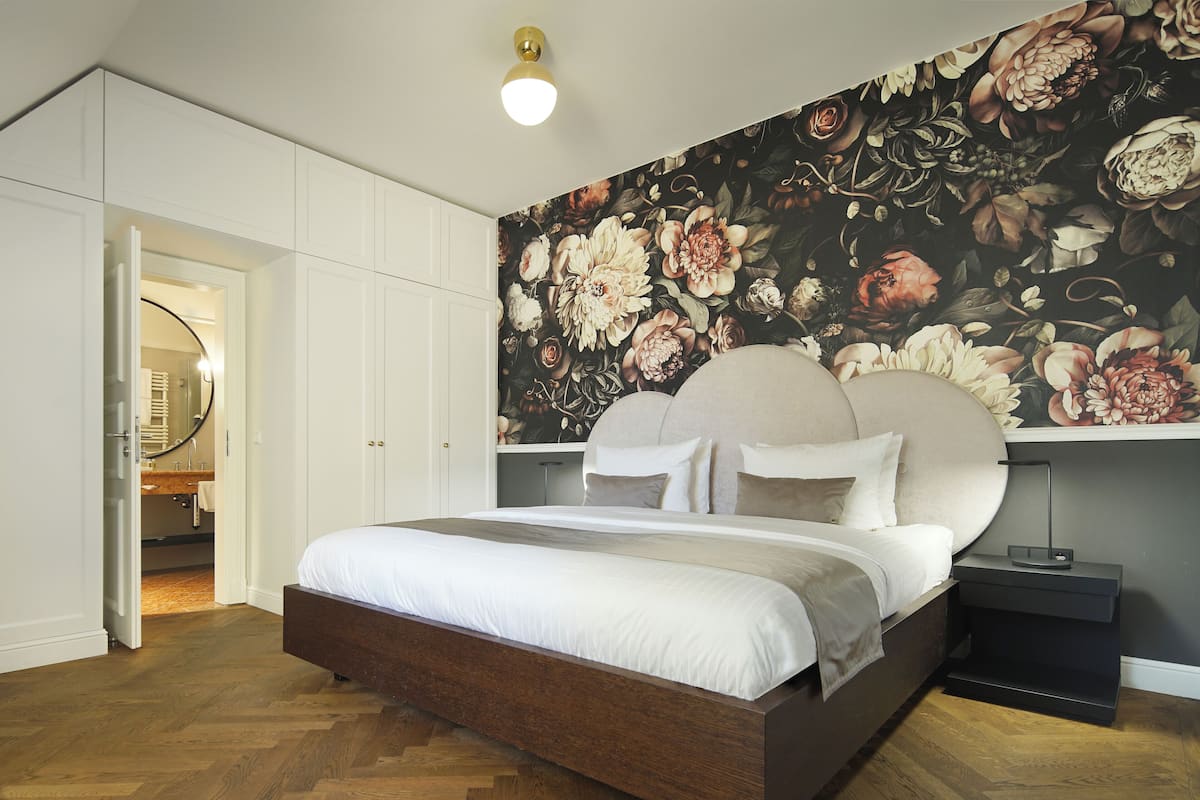 A bedroom with a large bed, a headboard, a nightstand, and a wall with a floral mural.