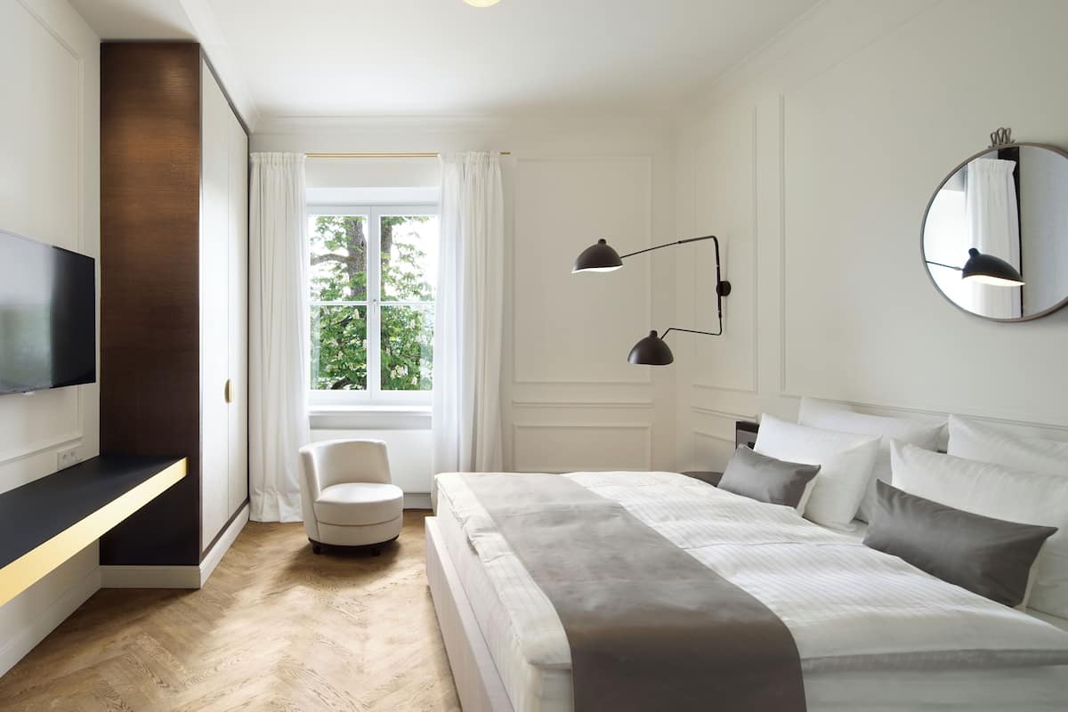 A modern bedroom with a bed, bedside lamps, a TV, and a window with curtains.