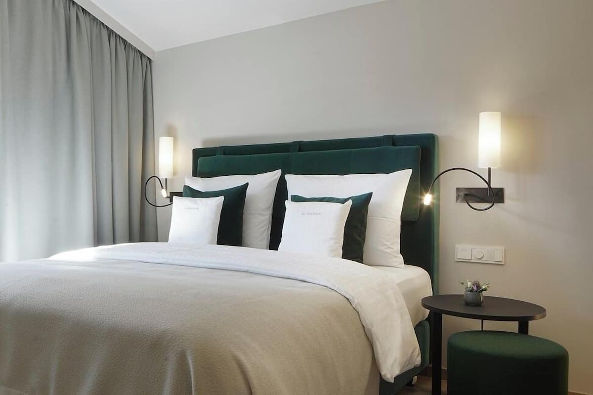 A neatly made bed with a green upholstered headboard, two bedside lamps, and a small round table with a plant.