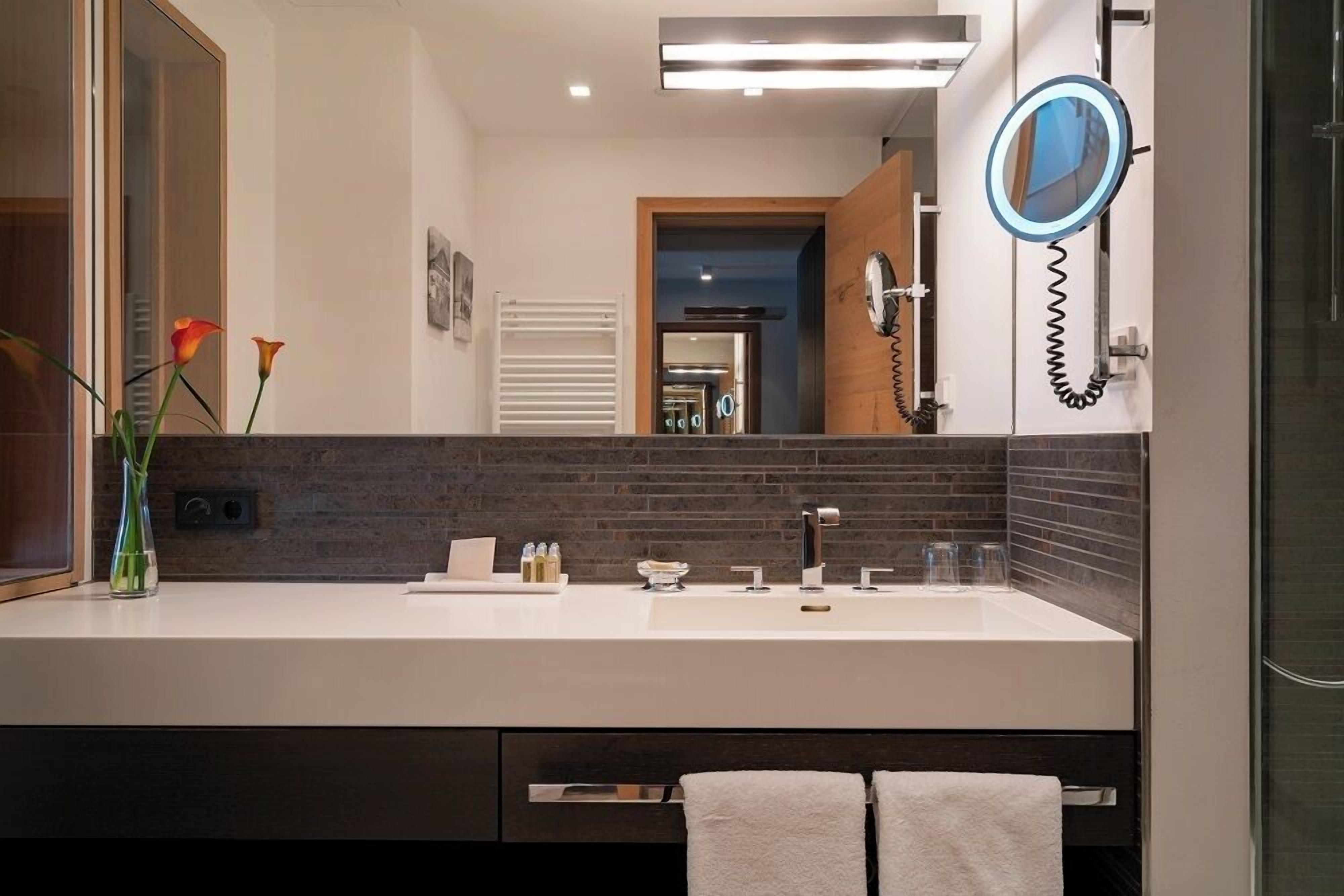 A modern bathroom with a large mirror, a white sink, and a towel rack.