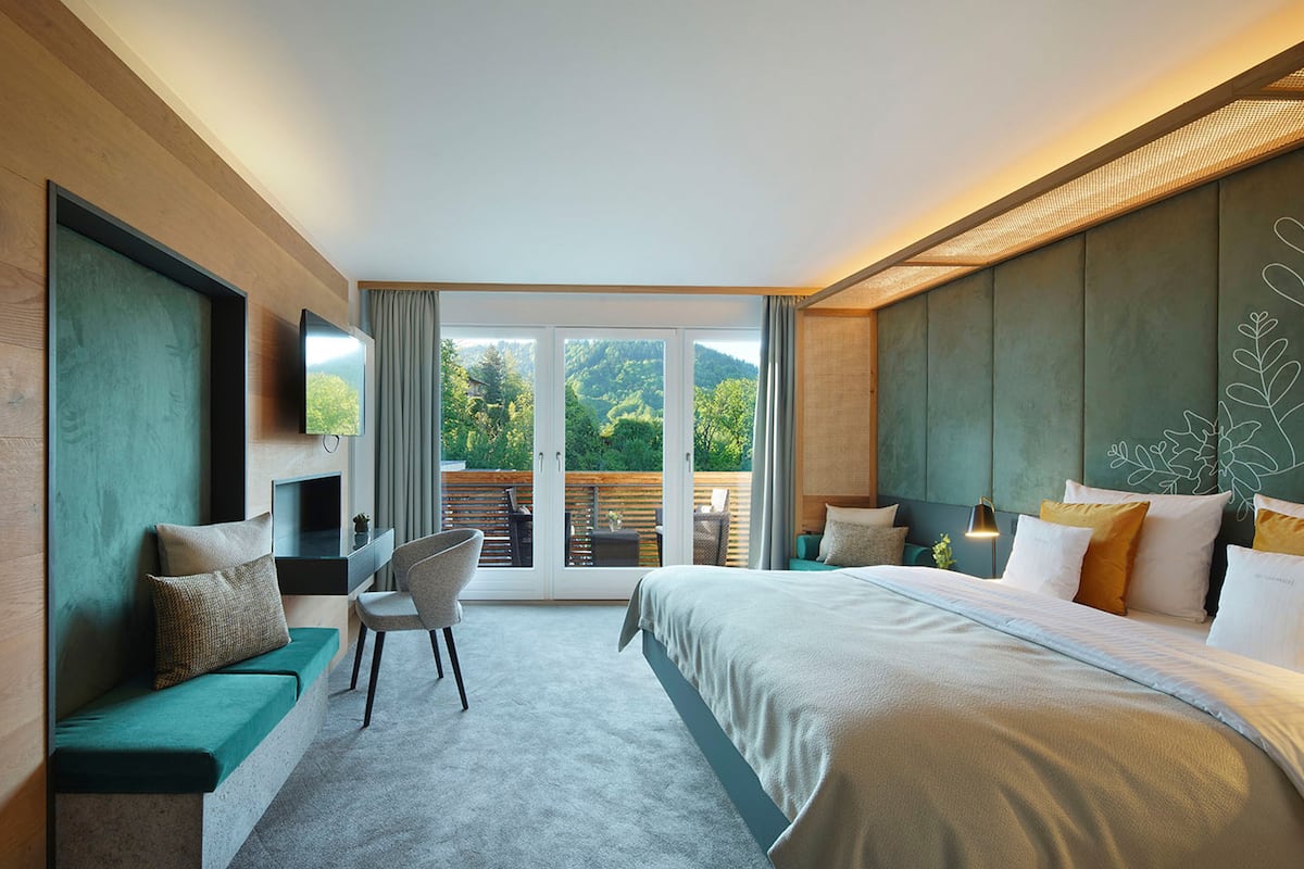A modern hotel room with a large bed, a desk, and a view of the outdoors.