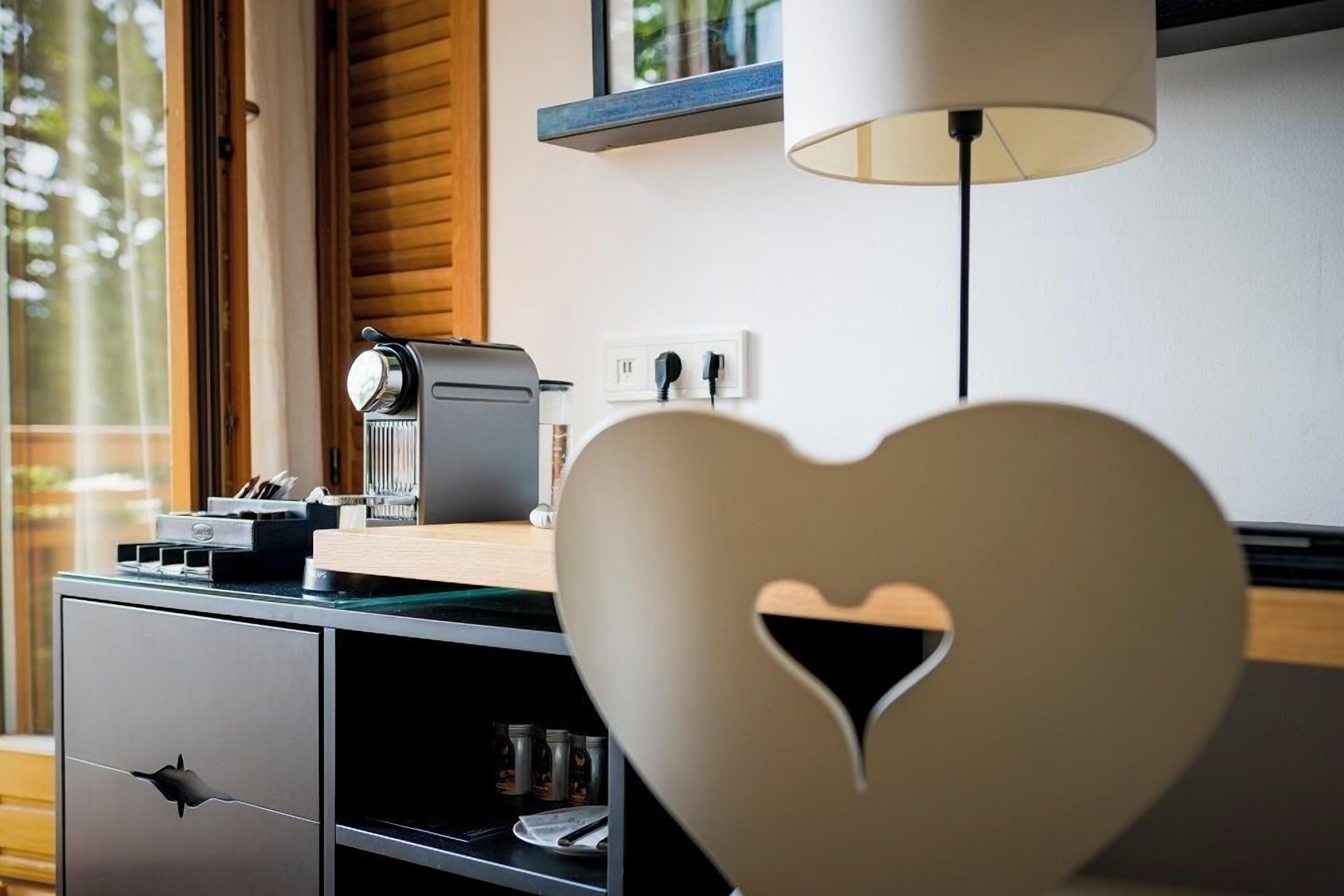A modern kitchen with a coffee machine, a heart-shaped cutout on a cabinet, and a window with blinds.